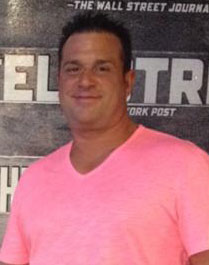 A man in pink shirt standing next to a wall.